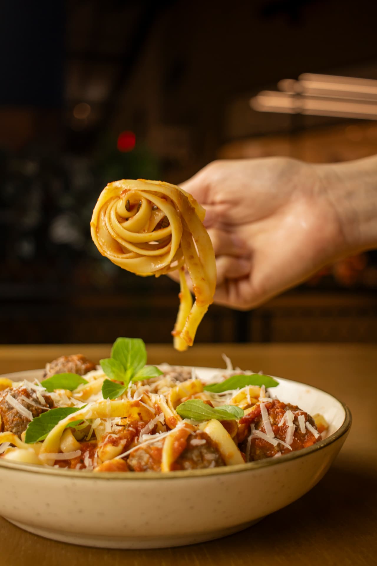 Hand twirling fettuccine with meatballs and parmesan on a fork