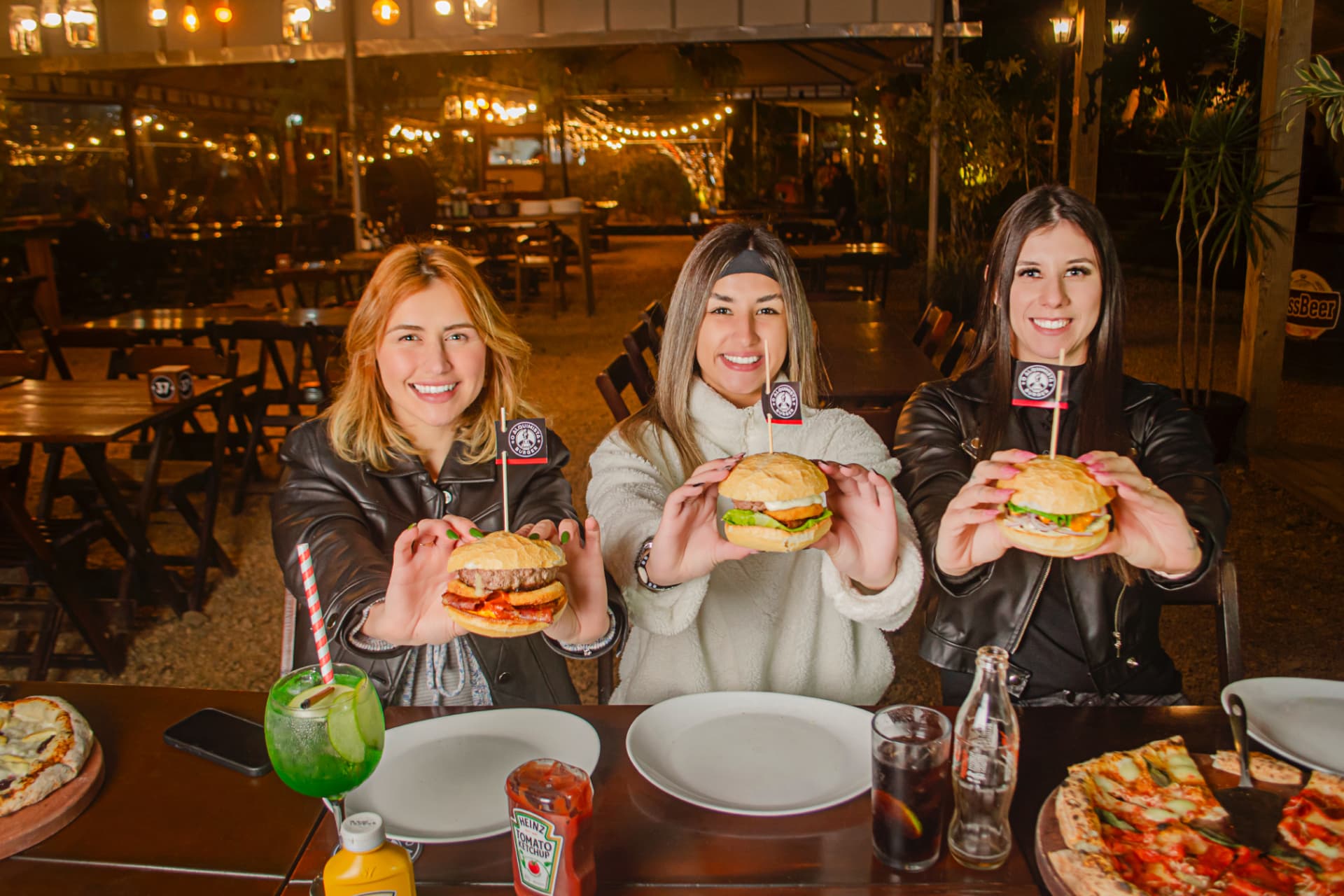 Guests holding artisanal burgers at the Jardim Alquimista garden